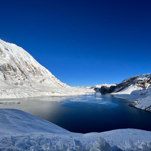 Breathtaking winter scene of a snowy alpine landscape with a tranquil lake and clear blue sky.