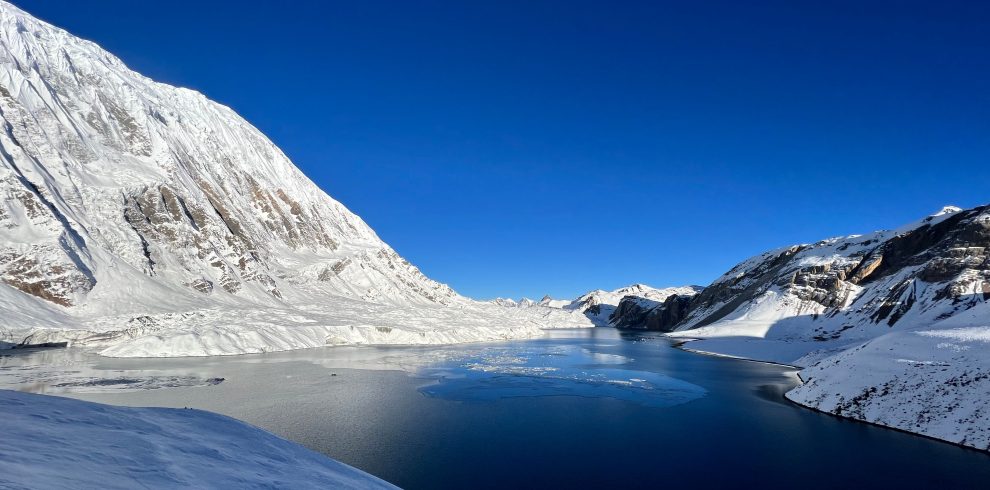 Breathtaking winter scene of a snowy alpine landscape with a tranquil lake and clear blue sky.