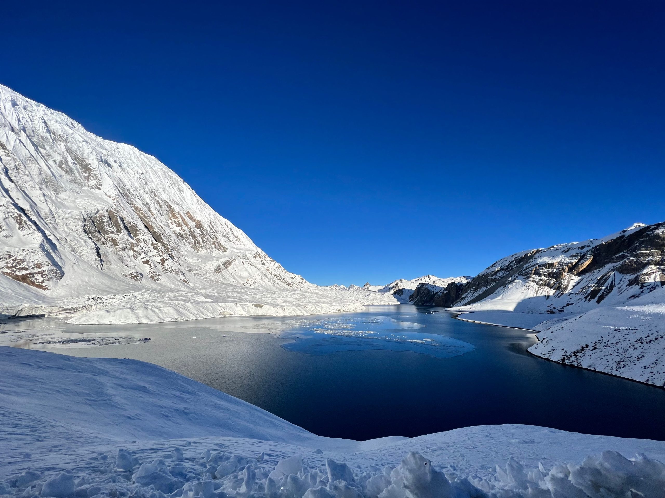 Breathtaking winter scene of a snowy alpine landscape with a tranquil lake and clear blue sky.